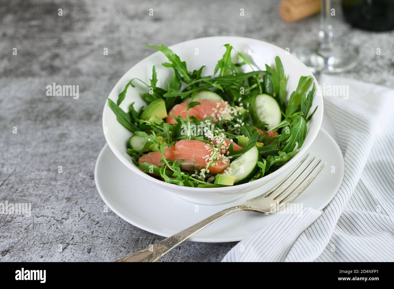 Vegetable salad from arugula, avocado and cucumber pieces with the addition of tender salted salmon, seasoned sesame seeds Stock Photo