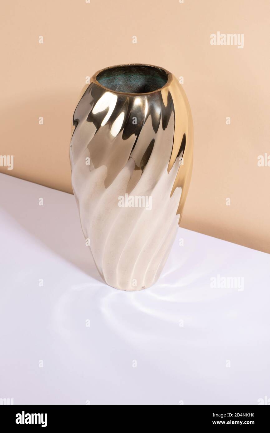 A vintage brass vase with a lot of shine and curved edges standing on a white table and a beige background. Mid century modern style, gold interior ob Stock Photo