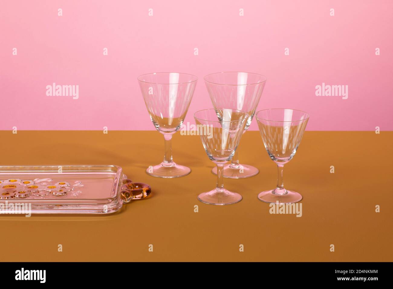 Set of classsic martini cocktail glasses standing next to a glass serving plate on a brown surface and a pink background. Clean minimalistic elegant s Stock Photo