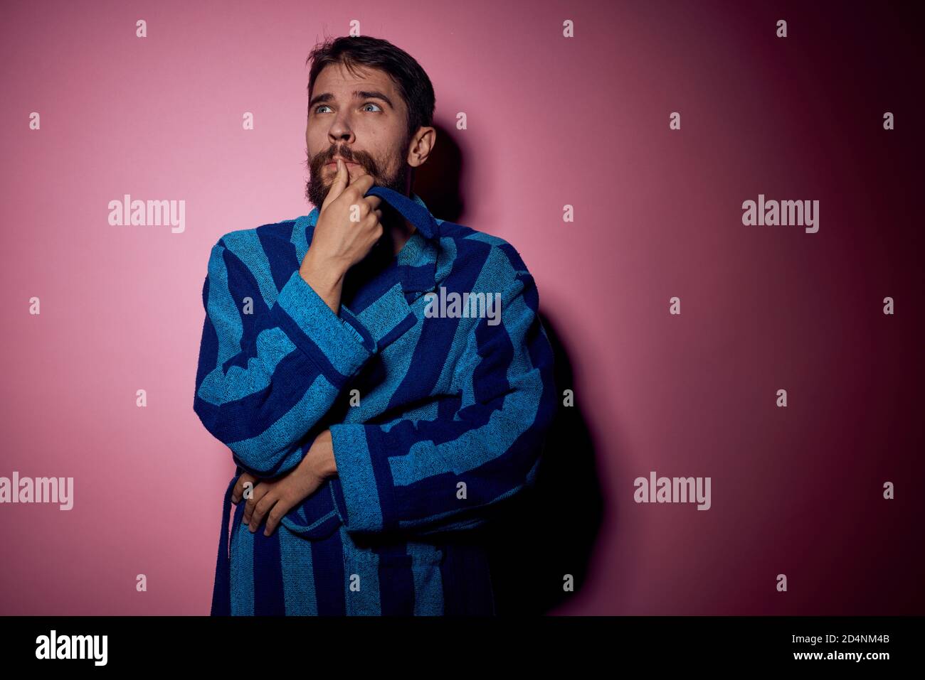 Bearded man in a blue striped robe on a pink background with hands ...