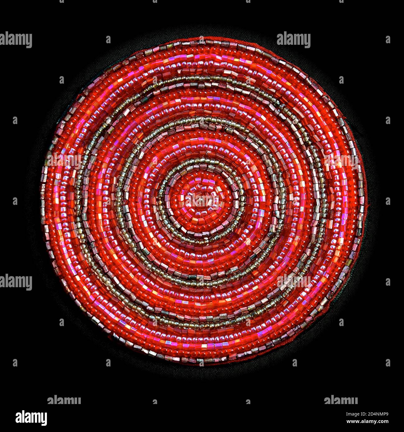 Macro image of a circular pink beaded coaster with small, glass iridescent beads sewn in concentric circles, isolated on a black background. Stock Photo