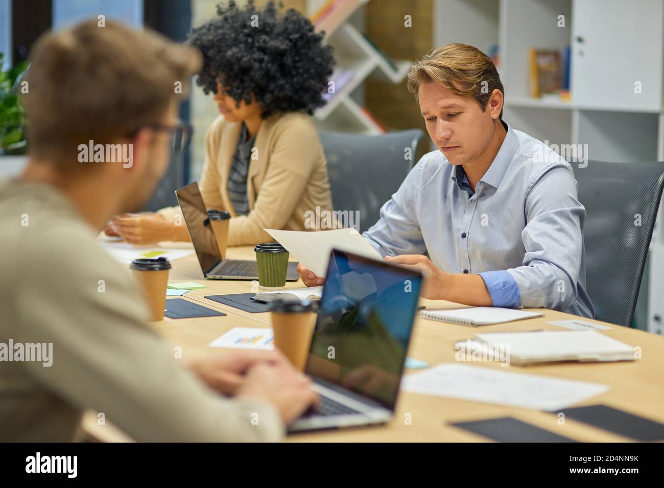 Office life. Three young multiracial business people sitting at desk in the board room and working on project together, using laptop and discussing work. Teamwork, collaboration and business concept Stock Photo