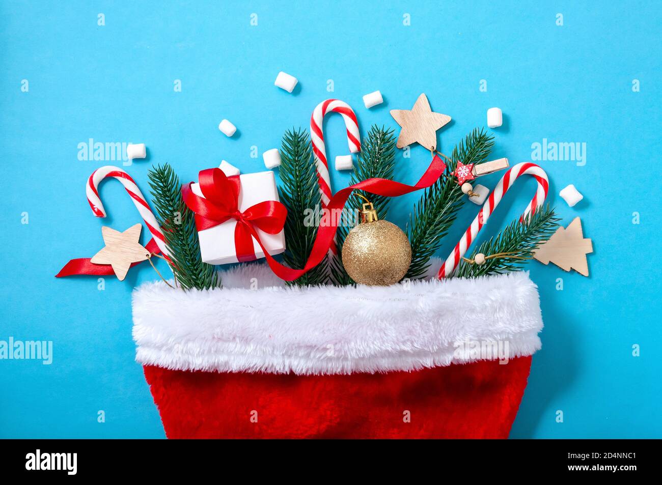 Creative Christmas Concept with Santa Hat, Fir Tree, Gift Box, Ball and Candys on Blue Background. Top View. Flat Lay. Stock Photo