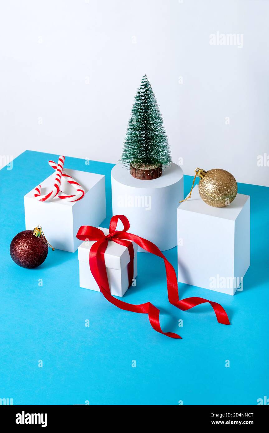 Creative Minimal Christmas Concept with Fir Tree, Gift Box, Ball and Candys on Different Geometrics Podium. Stock Photo
