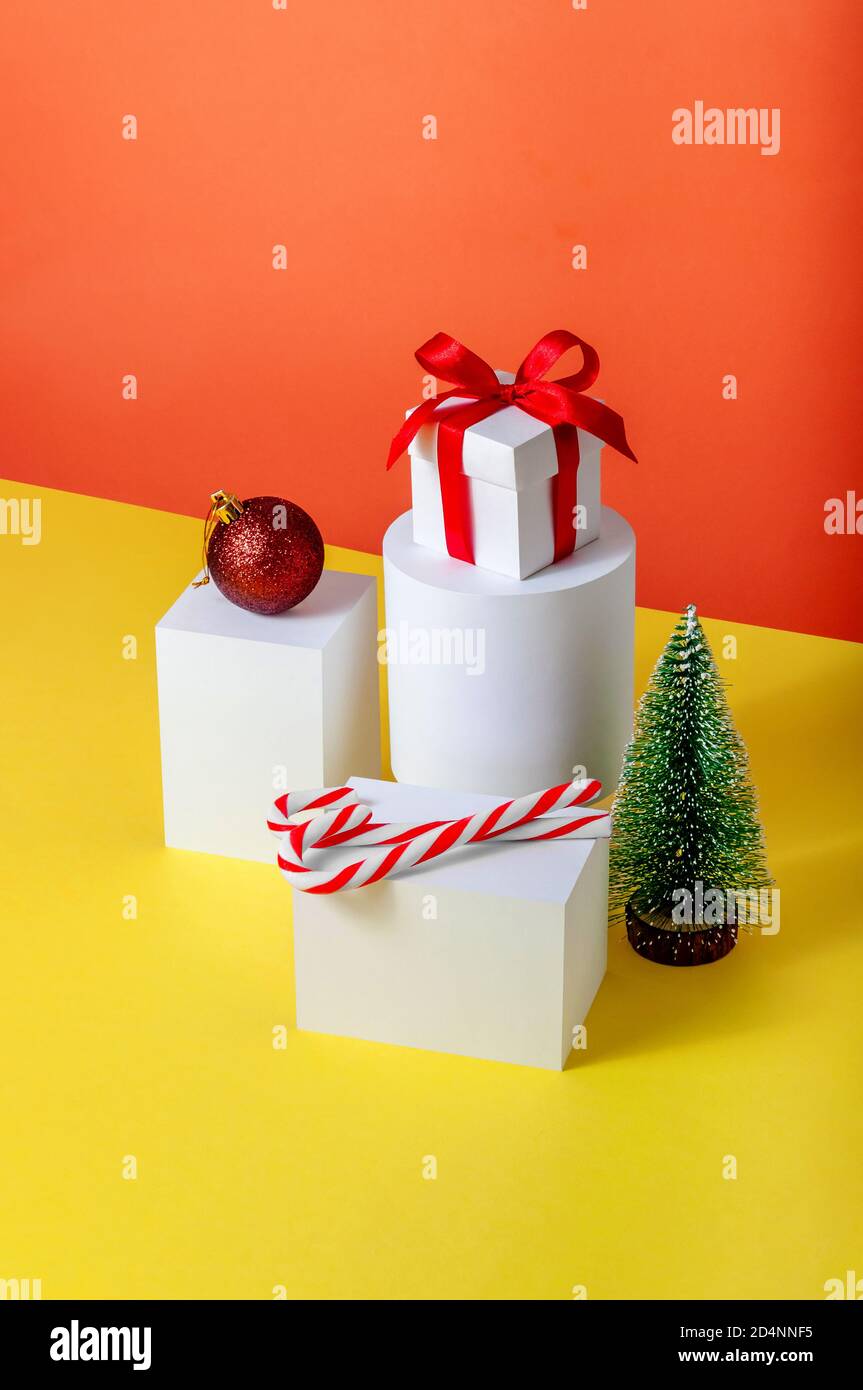 Creative Minimal Christmas Concept with Fir Tree, Gift Box, Ball and Candys on Different Geometrics Podium. Stock Photo