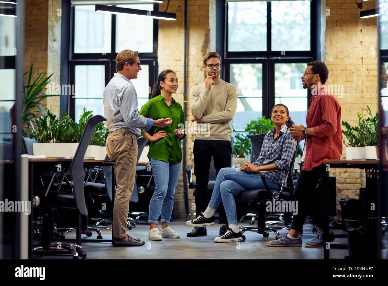 Brainstorming meeting. Group of young diverse multi ethnic business people standing together in modern office, sharing ideas and discussing work, full length. Business, teamwork, cooperation concept Stock Photo