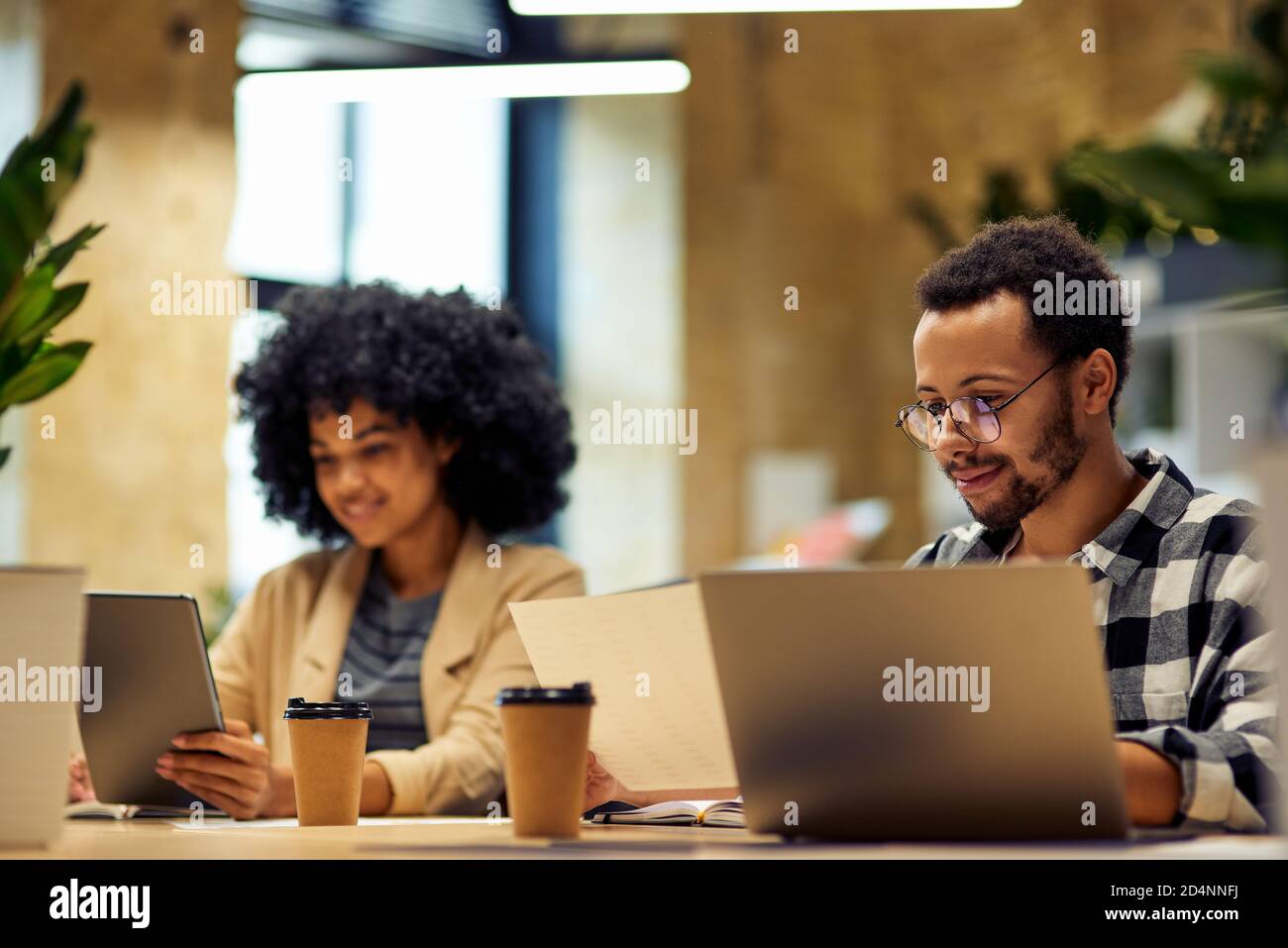 Using modern technologies. Two young multiracial business people sitting at the desk, working together in coworking space. Office life, teamwork and business Stock Photo