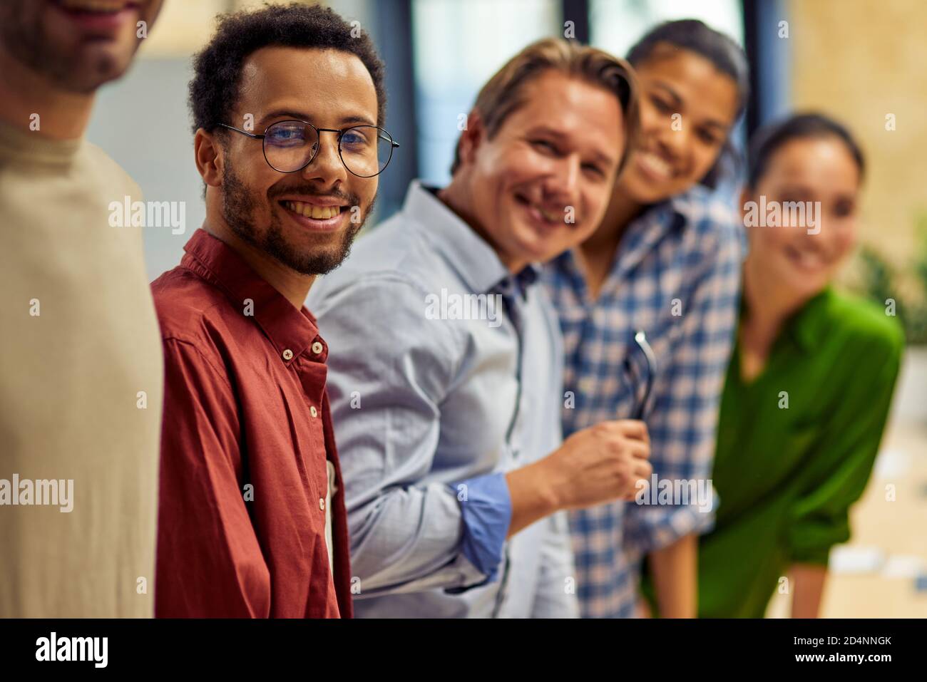 Successful team. Group of young happy multi ethnic business team looking at camera and smiling while standing in the modern office, working together. Business, teamwork, cooperation Stock Photo