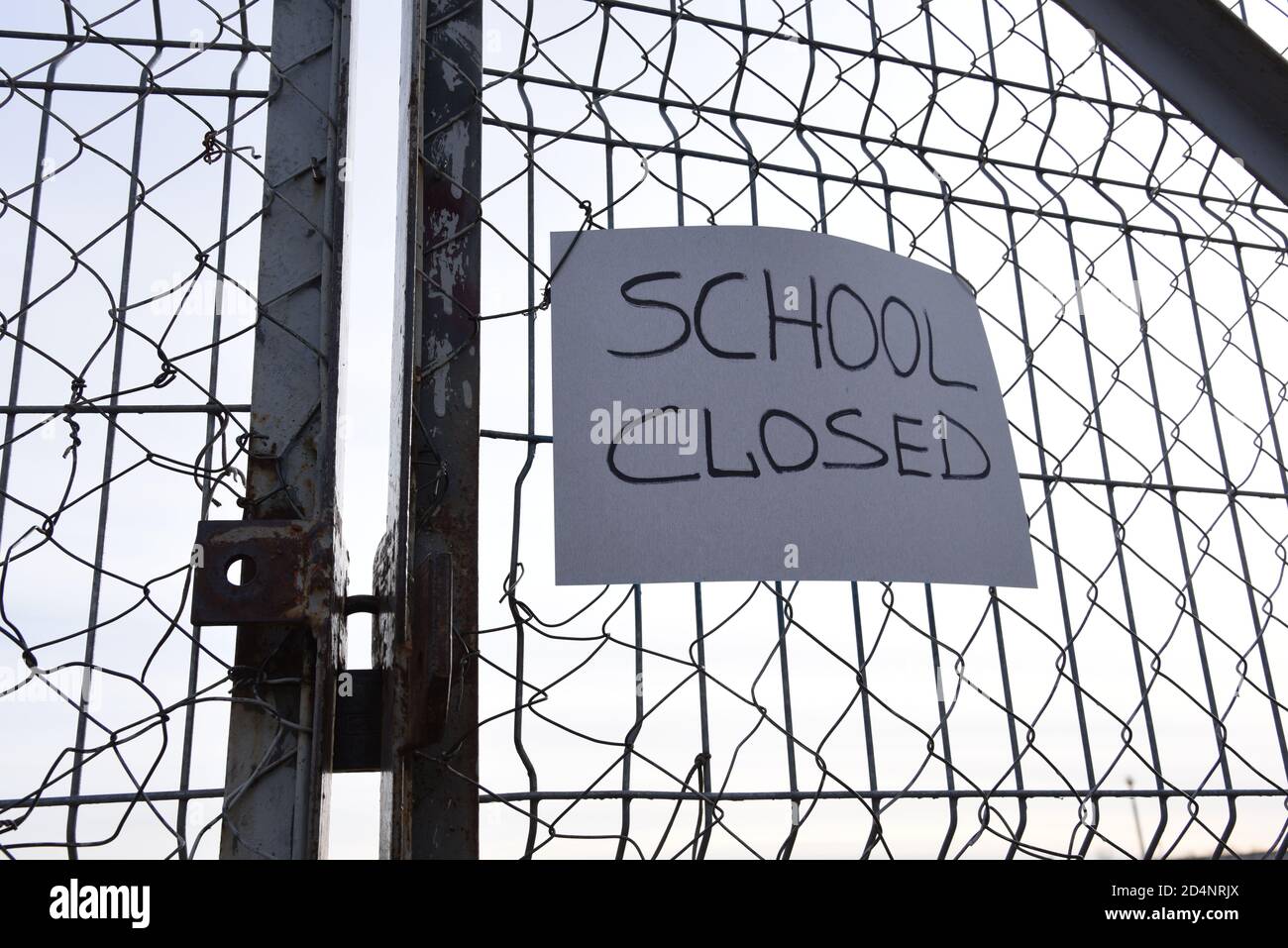 SCHOOL CLOSED text on the yellow plate on a mesh wire fence. Quarantine Area. Students out of schools or universities because of outbreak COVID-19 pan Stock Photo
