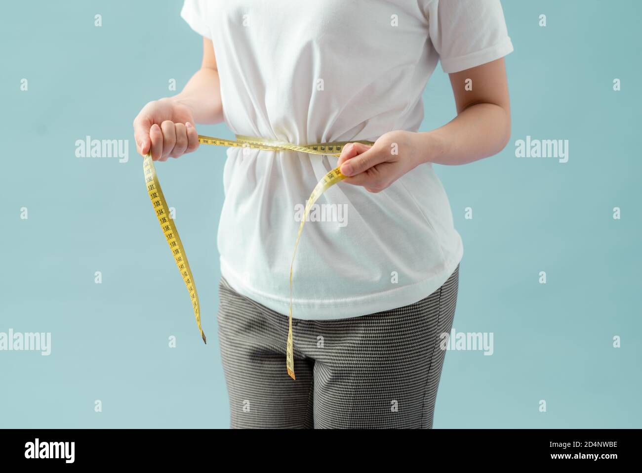 Weight loss, slim body, healthy lifestyle concept. Fit fitness girl measuring her waistline with measure tape on blue Stock Photo