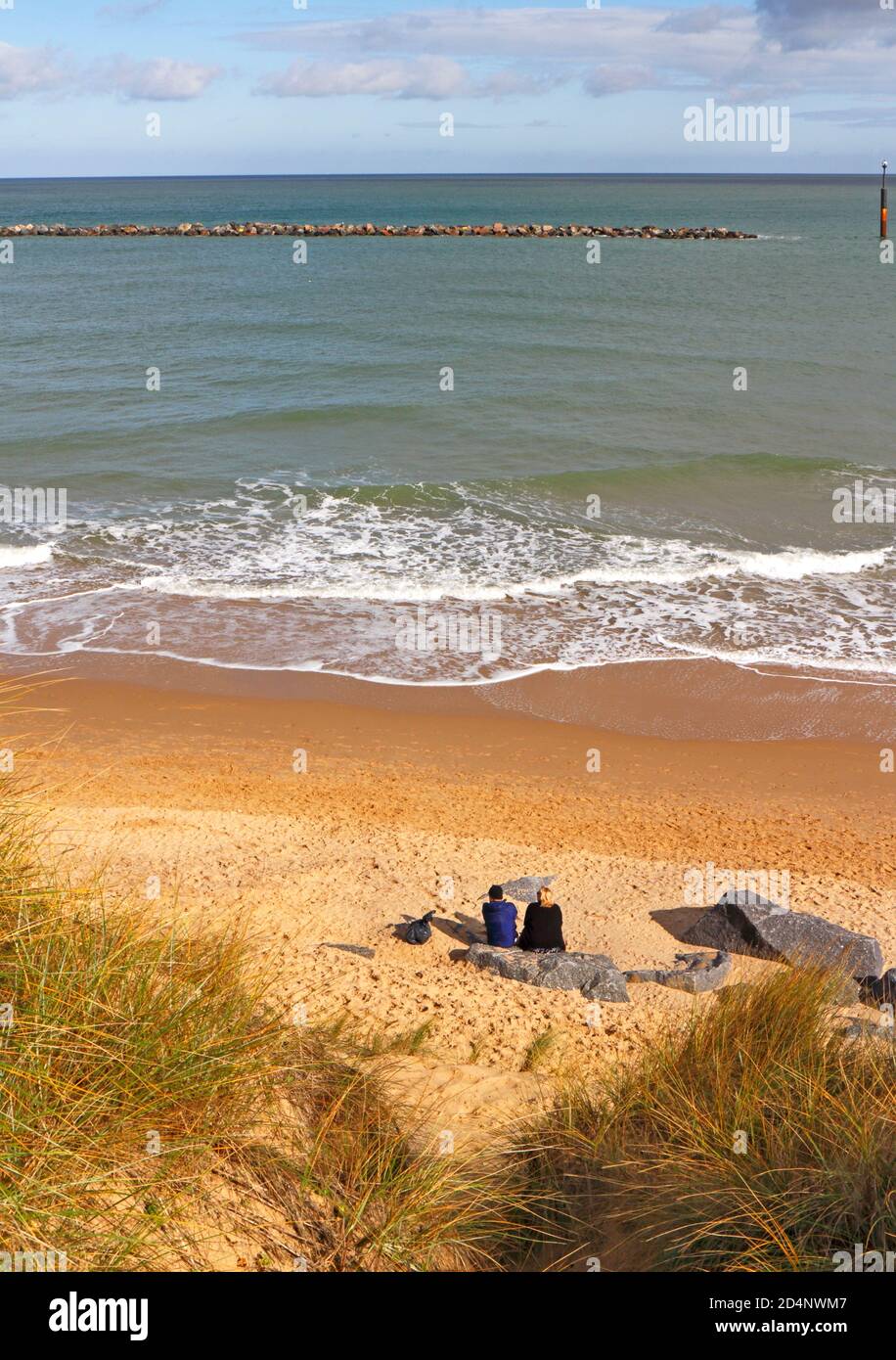 A couple sitting on a rock looking out to sea from a beach on the Norfolk coast at Sea Palling, Norfolk, England, United Kingdom. Stock Photo