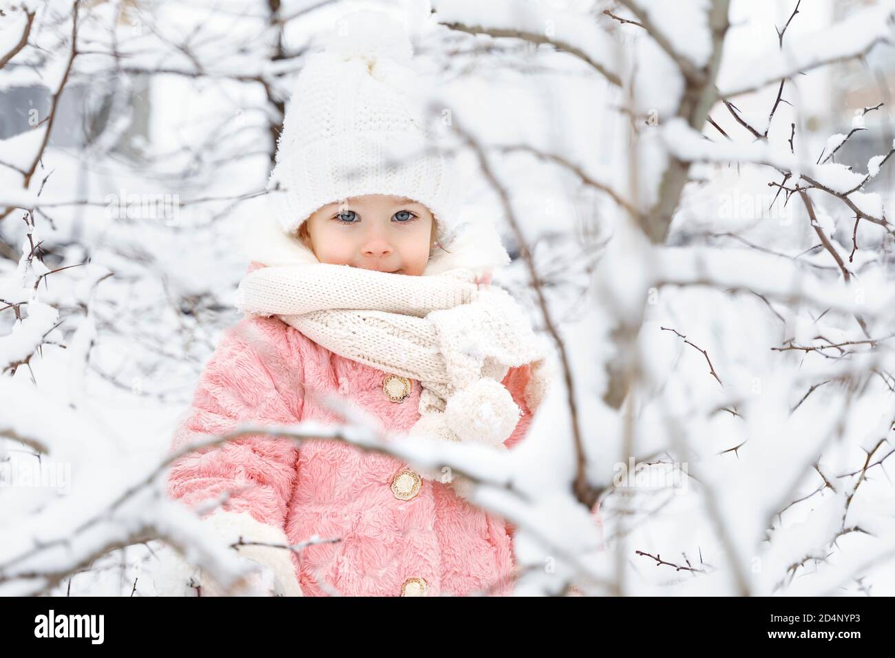 beautiful little girl in a pink fur coat and a knitted hat among the ...
