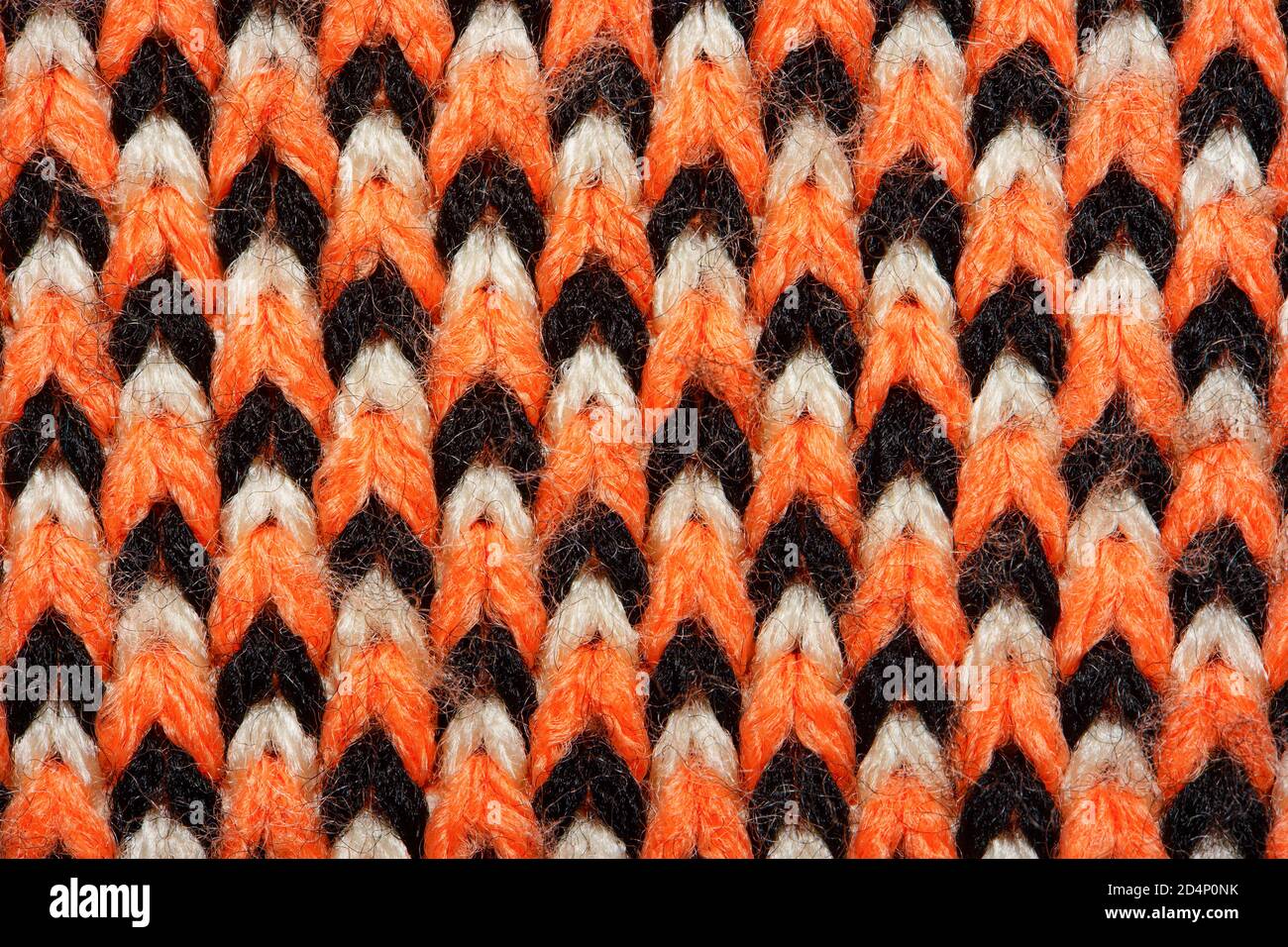 Synthetic knitted fabric with pattern elements of red, black and white yarns close up. Multicolor patterned knitted fabric texture. Background Stock Photo