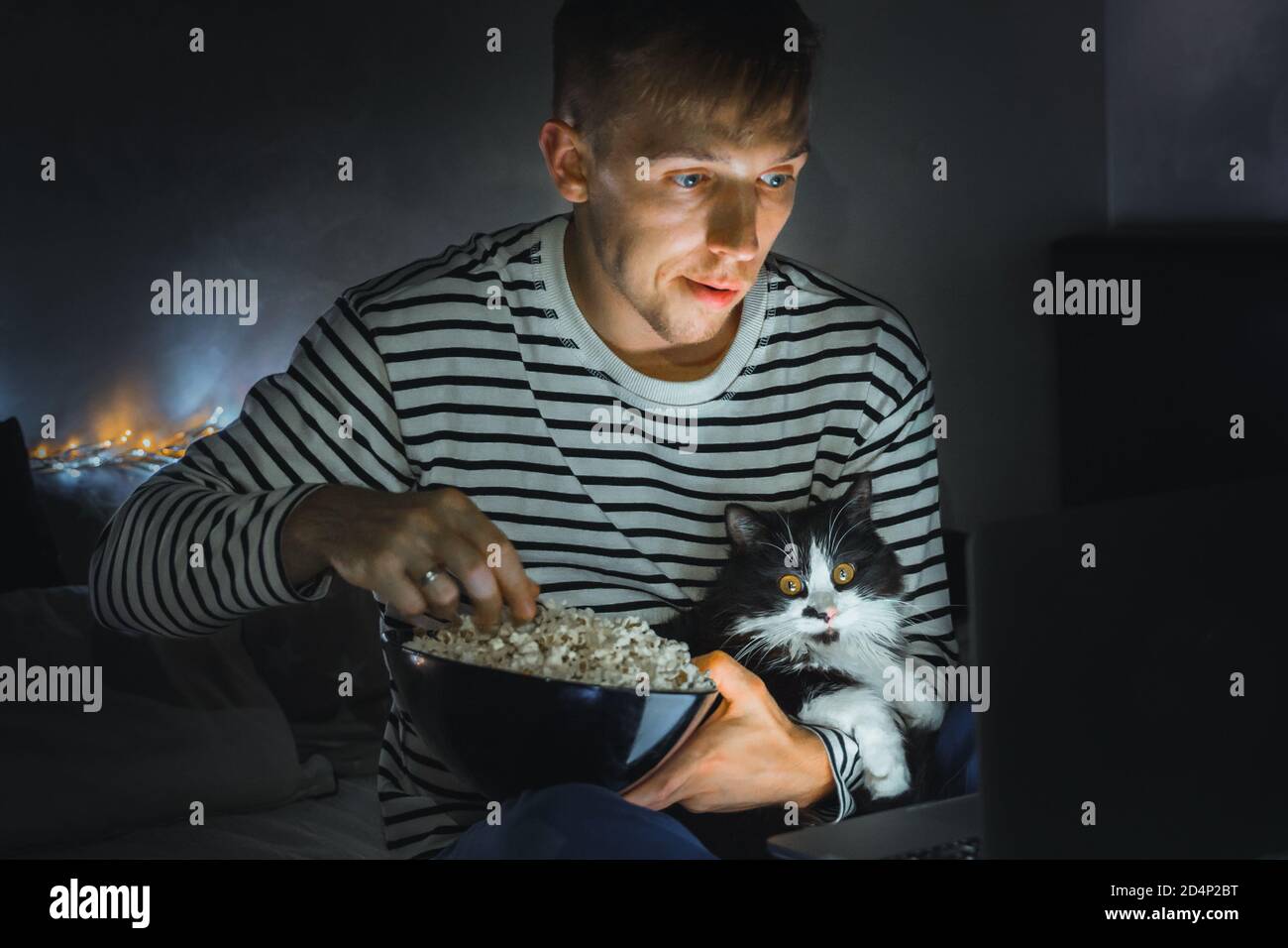 young man with black cat watching a movie eating popcorn on TV at