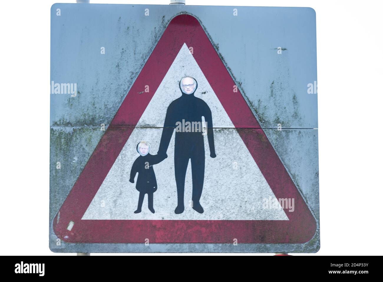 Political comment made by adding faces of Boris Johnson and Dominic Cummings to adult and child crossing, pedestrians in road traffic sign Stock Photo
