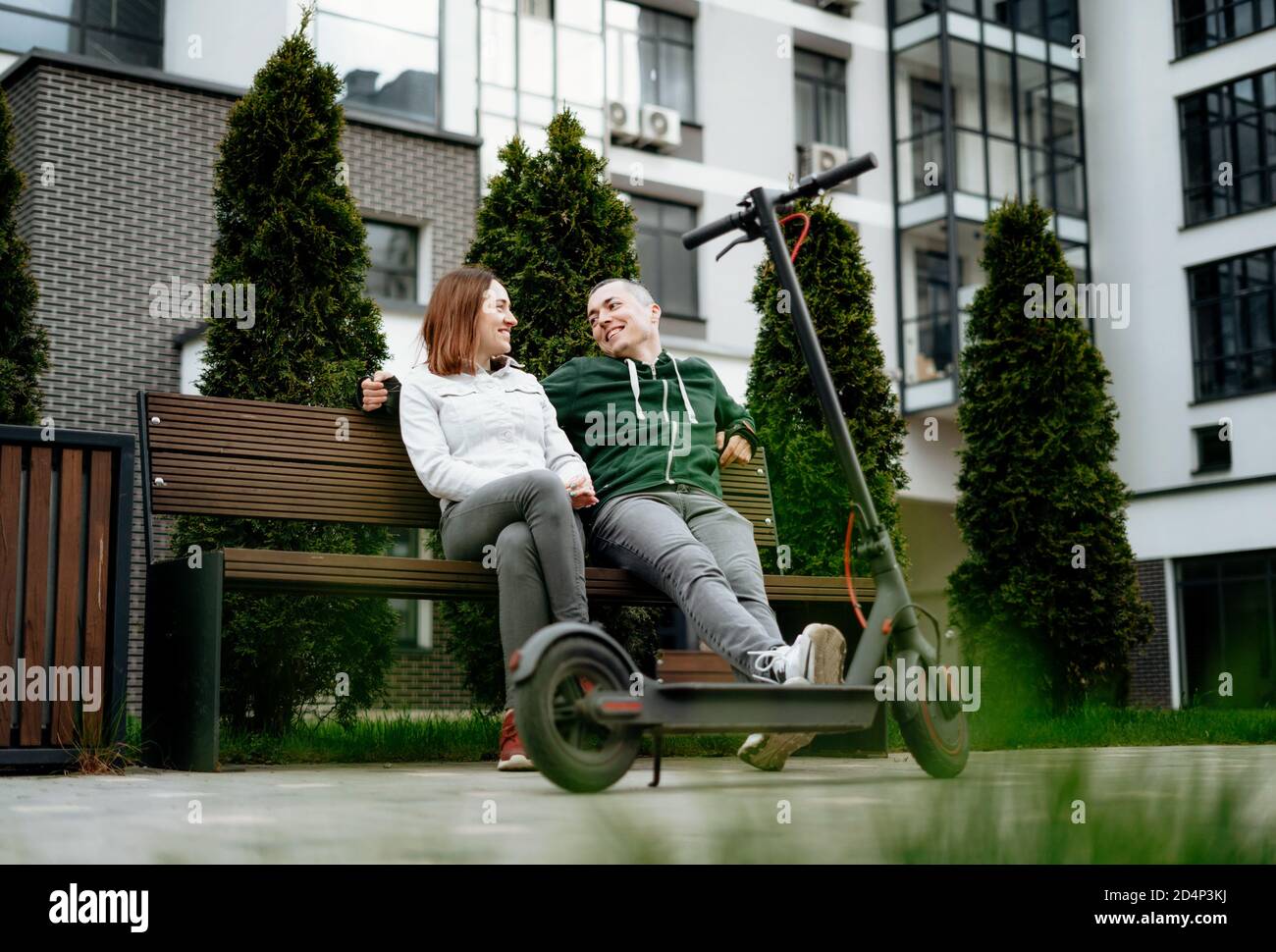 Couple sit next to electric kick scooter in street and laughing. Stock Photo