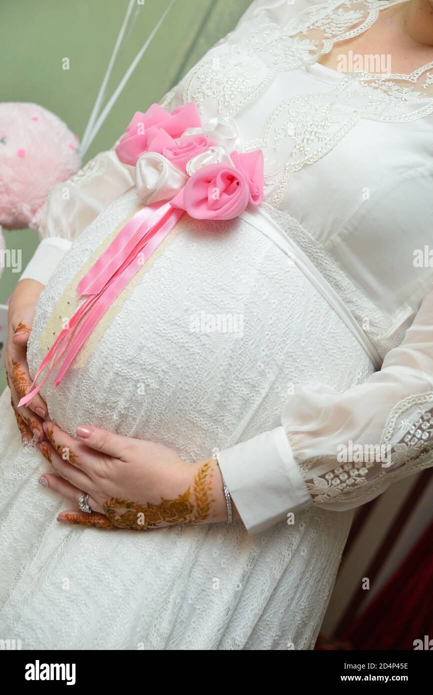 Pregnant woman in dress holds hands on belly . Pregnancy, maternity, preparation and expectation concept. Close-up, copy space, indoors. Beautiful ten Stock Photo