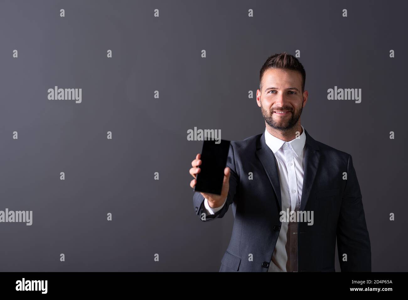 A smiling handsome young businessman in a suit showing the screen of a ...