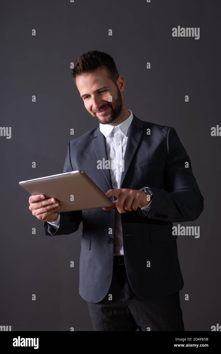 A smiling handsome young businessman in a suit using a tablet in front ...