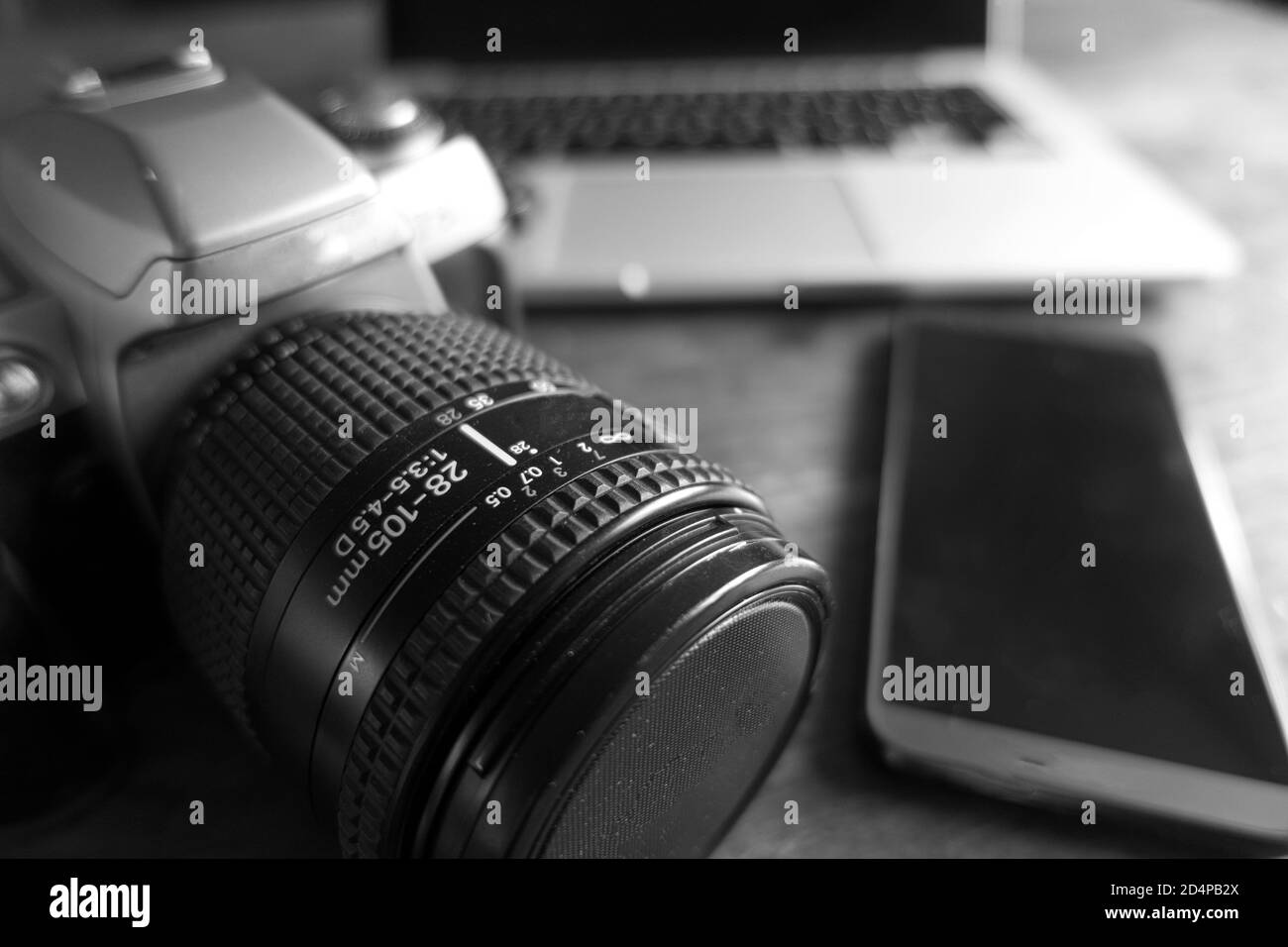 An old SLR 35mm camera placed on a coffee table next to a modern smartphone and laptop Stock Photo