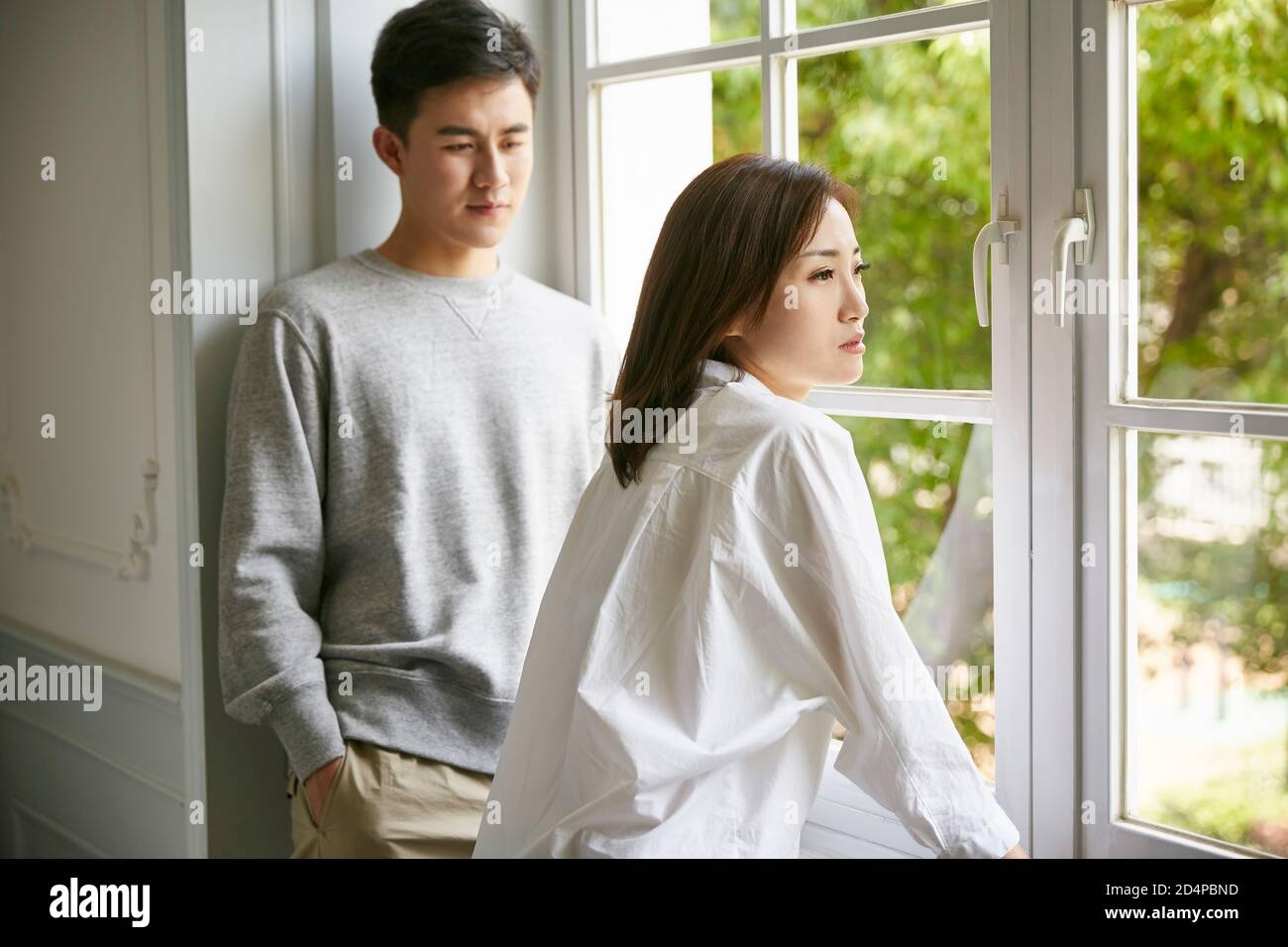 young asian couple standing by the window talking chatting during stay at home order Stock Photo