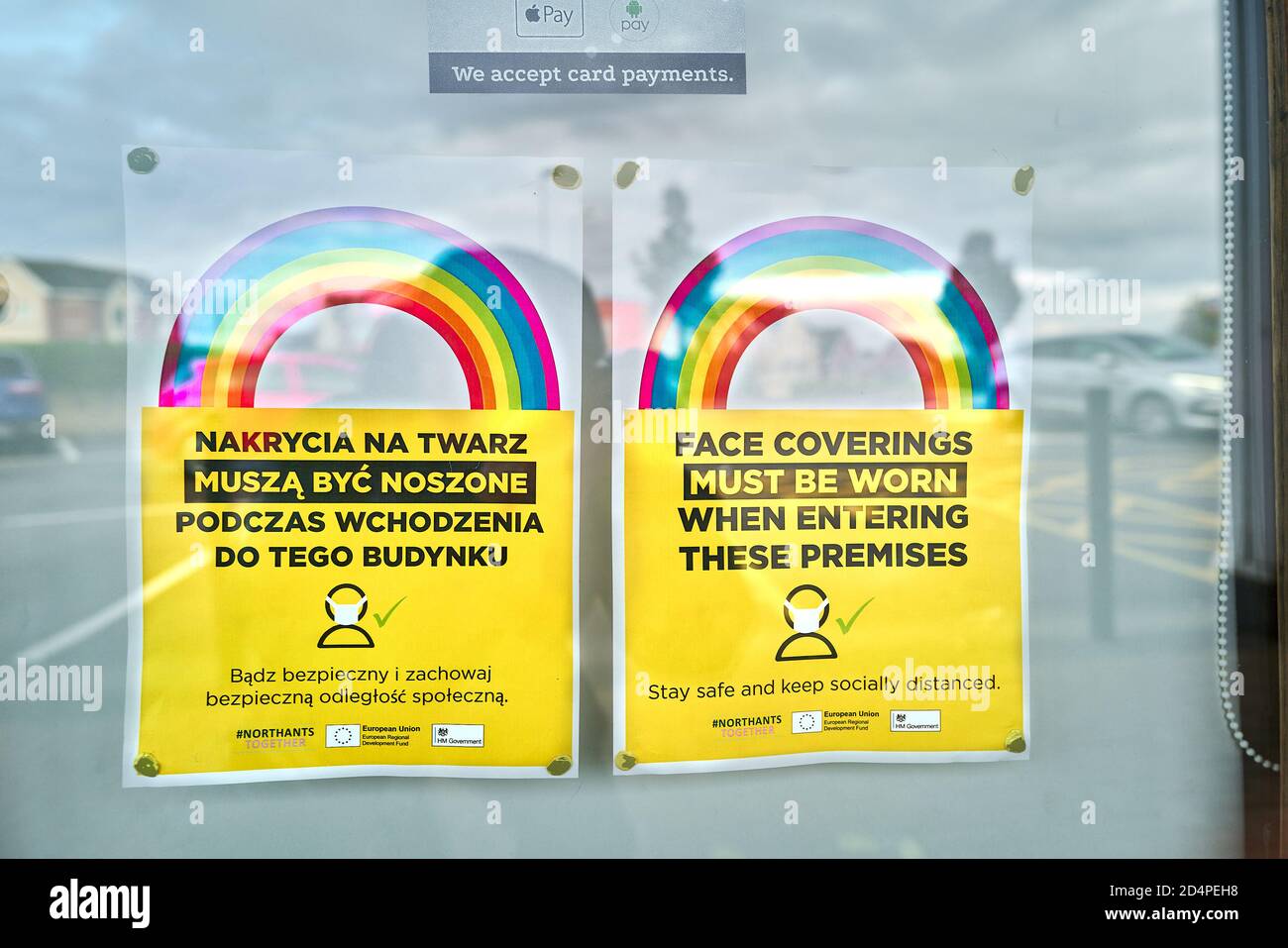 'Face coverings must be worn' notice (in english and polish) and the rainbow symbol in the window of a barber's shop at a shopping centre, Corby, Nort Stock Photo
