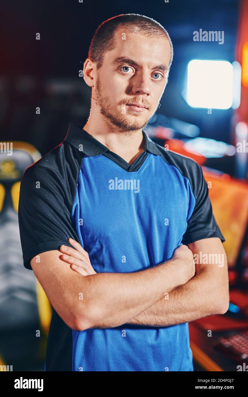 Playing online video games professionall. Young confident caucasian guy, male cyber sport gamer keeping arms crossed and looking at camera while participating in eSports tournament or competition Stock Photo