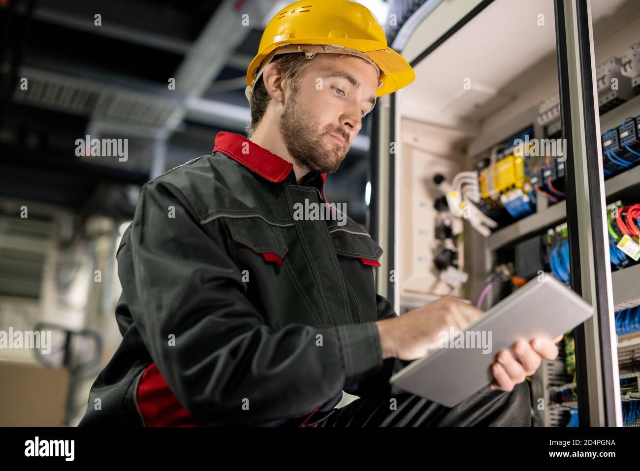 Young serious engineer in workwear and hardhat scrolling through technical data Stock Photo