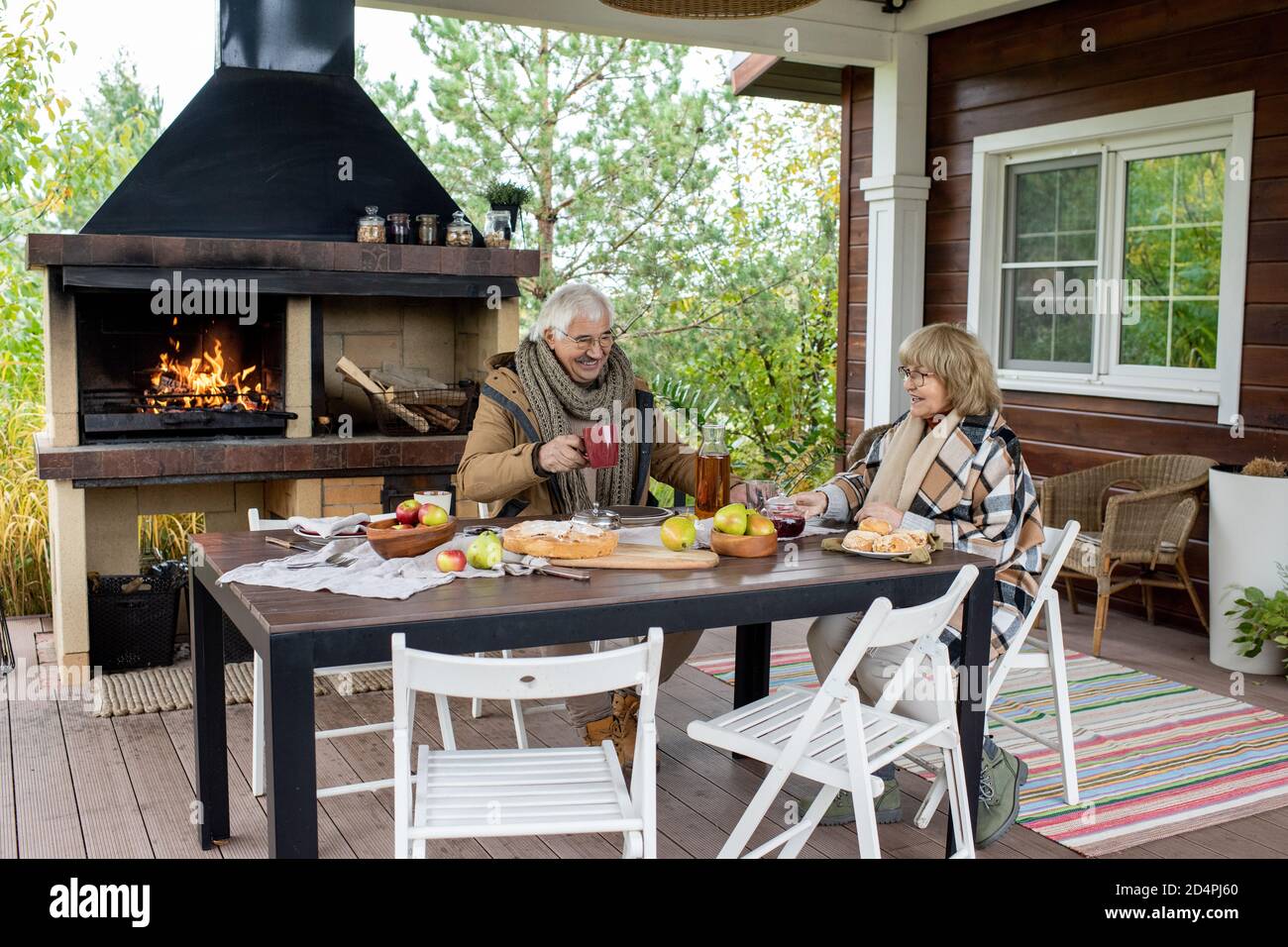 Cheerful senior couple in warm casualwear having tea by dinner table outdoors Stock Photo