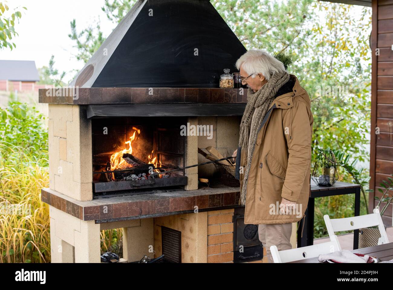 Contemporary senior man in warm casualwear standing by fireplace by house Stock Photo