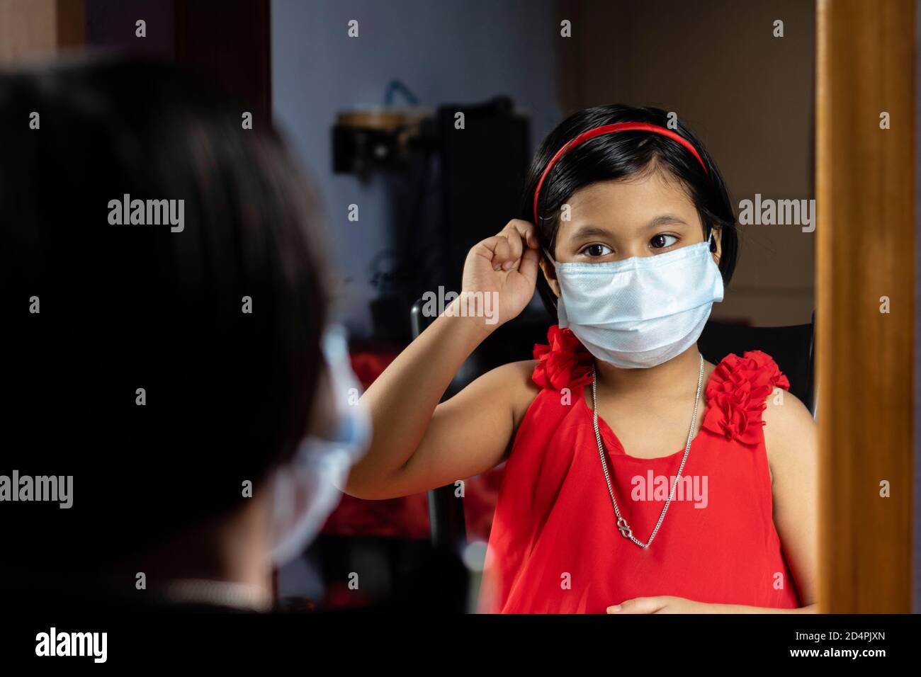 a cute Indian girl child in red dress adjusting surgical nose mask in