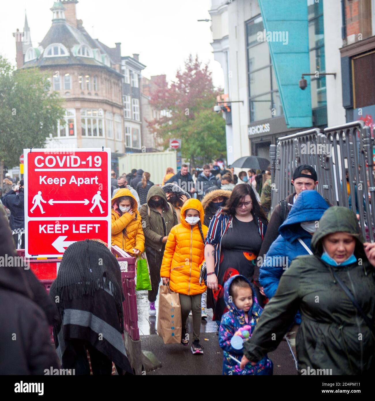 Covid-19 social distancing sign observed by shoppers in the rain. Stock Photo