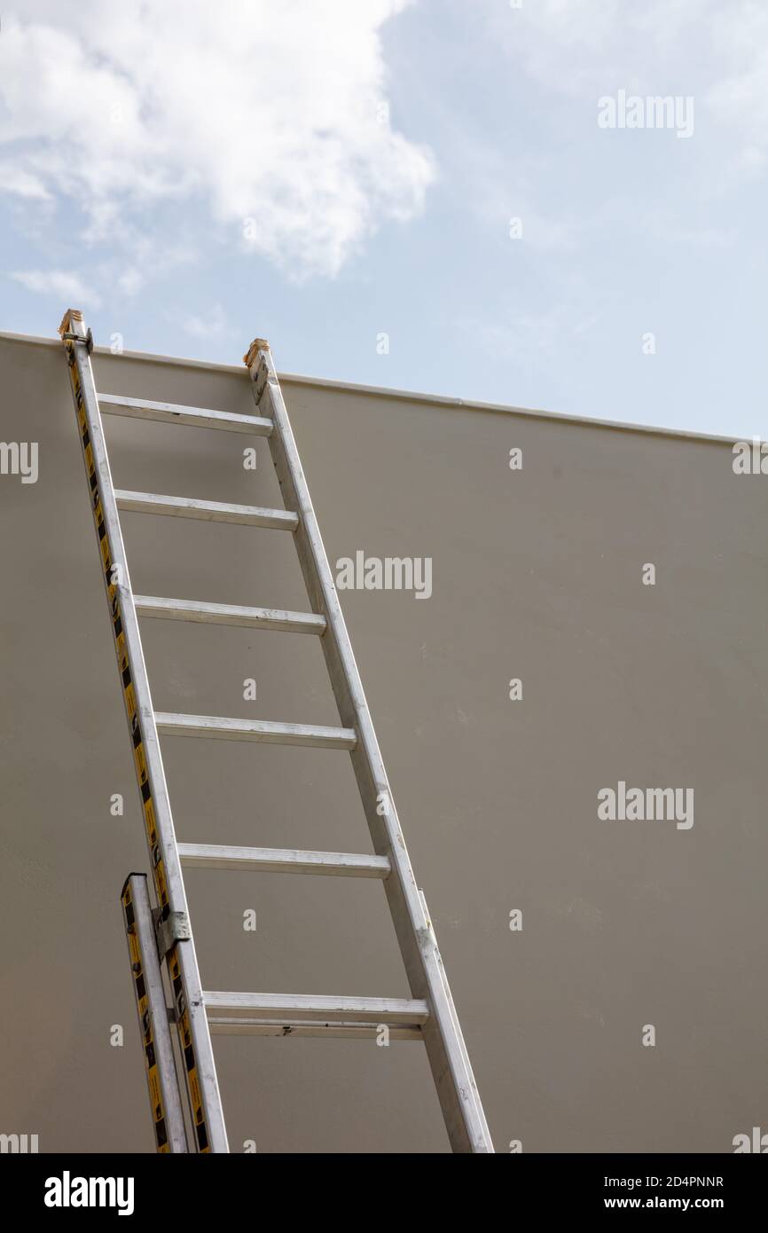 Maintenance concept. Ladder aluminium, light, silver color put on grey wall. Support for repairing with safety. Low angle view, vertical, blue sky bac Stock Photo