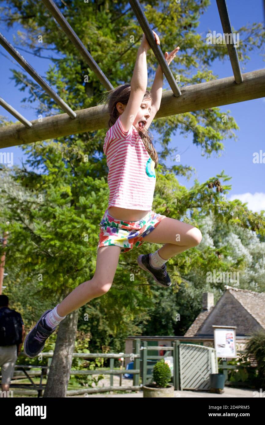 Young girl swinging across monkey bars at play park Stock Photo