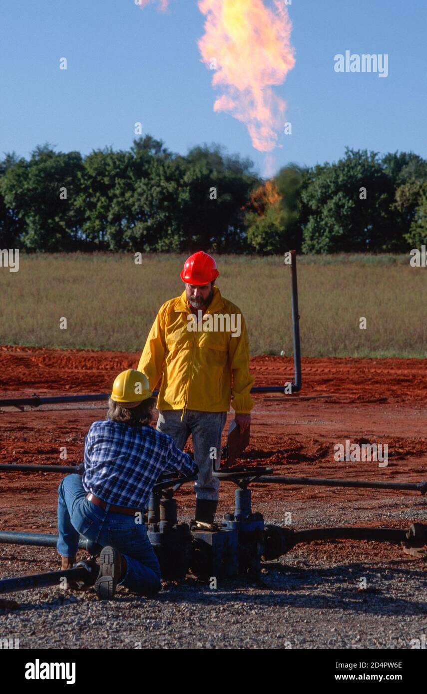 Worker adjusts valve at an Oklahoma oil field site While Engineer Supervises, USA Stock Photo