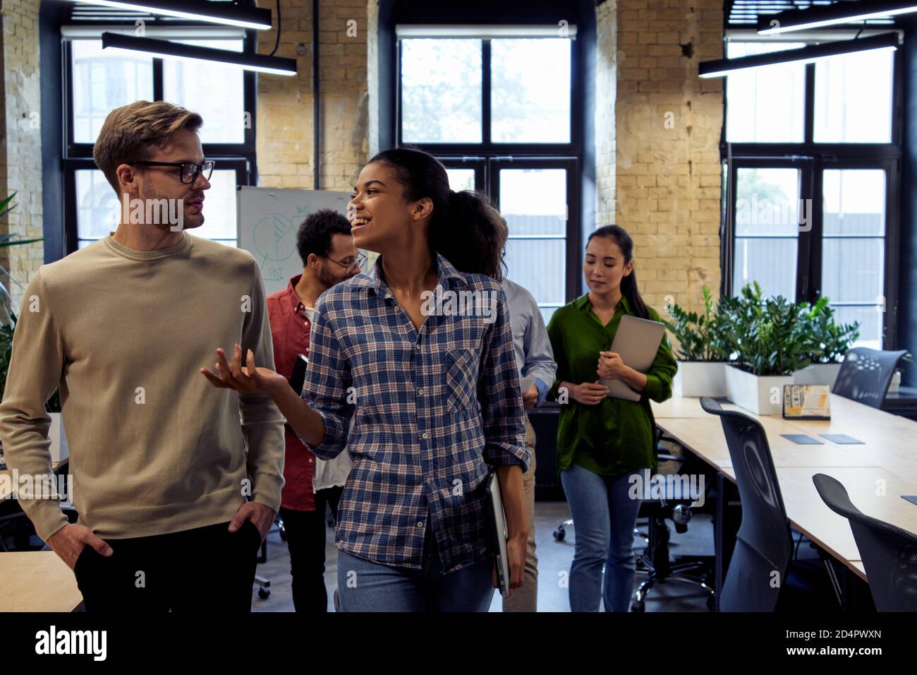 After team meeting. Two young diverse business people, male and female coworkers talking about something while walking in the modern office. Informal conversation at work Stock Photo