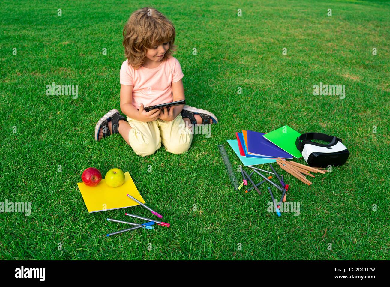 Elementary school students boy doing homework outdoor. Child reading tablet. Kids education, learning and studying. Stock Photo