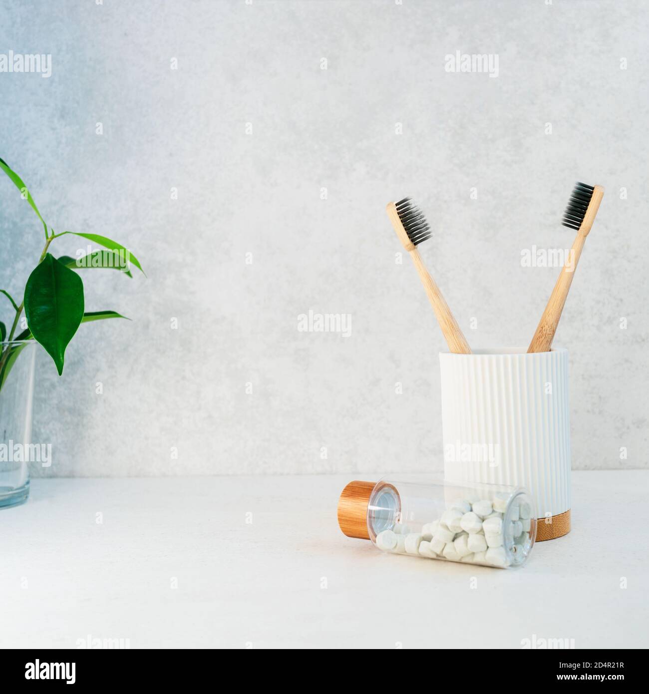 Zero waste bathroom items. Bamboo toothbrushes in recycling material holder, natural mouthwashing tabs and fresh green plants in glass. Oral care esse Stock Photo