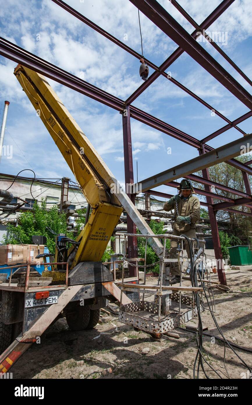 Shymkent, Kazakhstan - April 27, 2012: Welding worker on mobile crane craddle. Assembling of new industrial building structure. Stock Photo