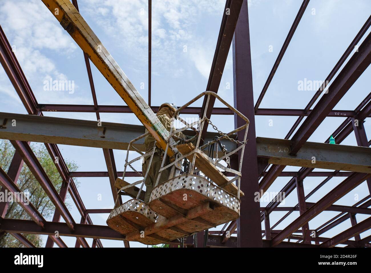 Welding worker on mobile crane craddle. Assembling of new industrial building structure. No face. Stock Photo
