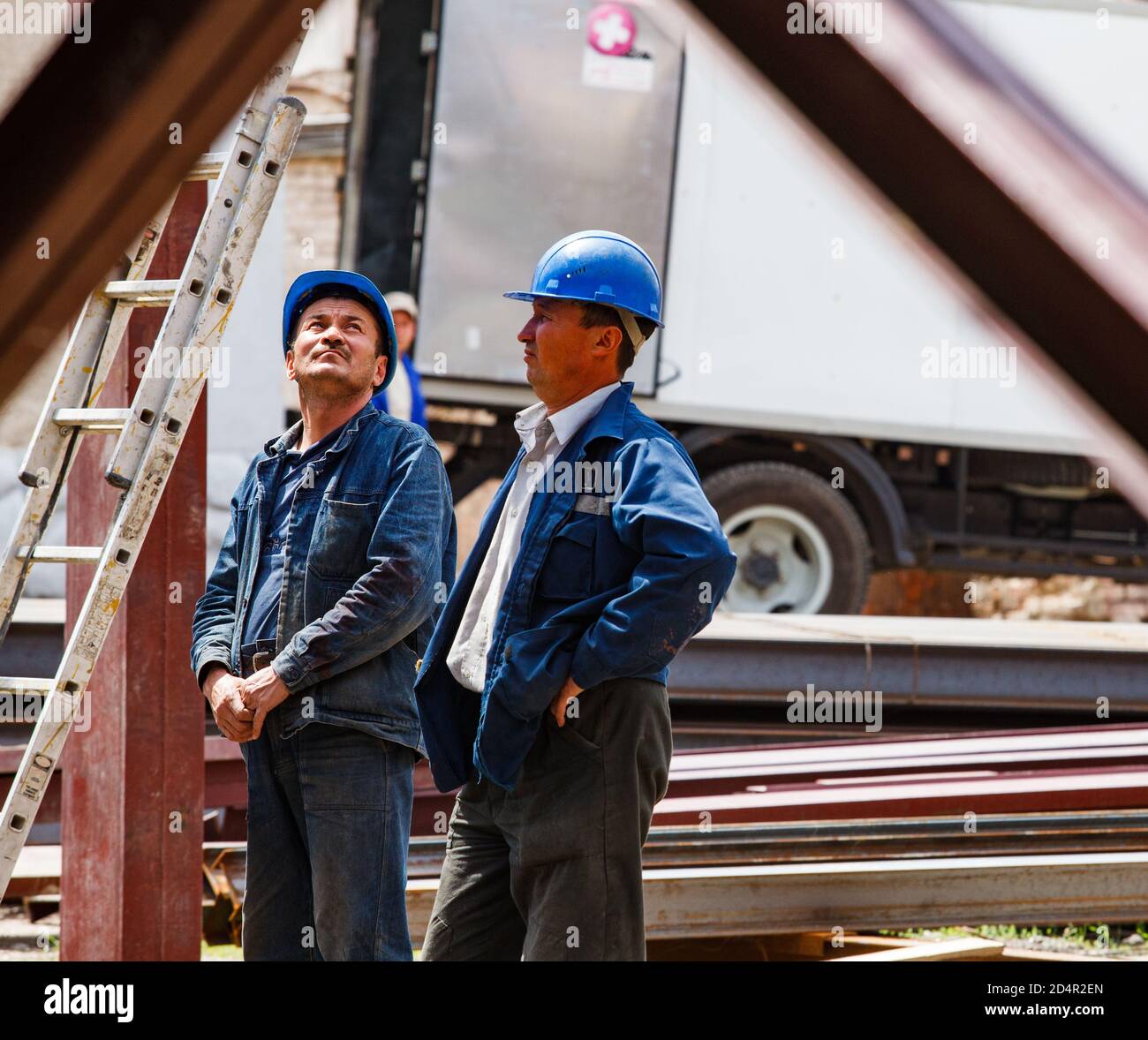 Shymkent, Kazakhstan: Two workers or engineers in blue hardhats talking. Stock Photo