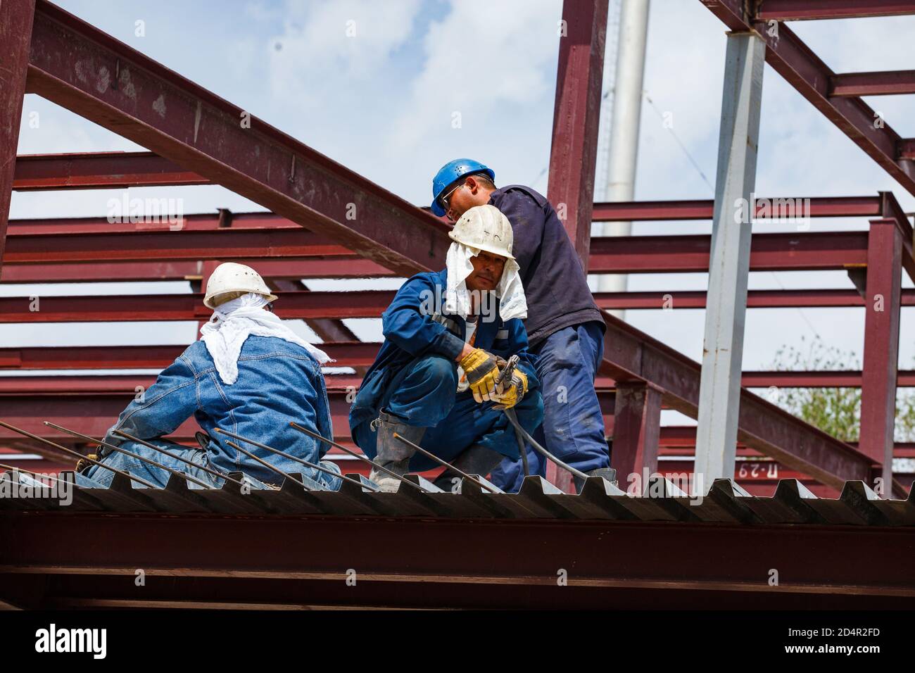 Shymkent, Kazakhstan. industrial building of chemical pharmaceutical plant Santo. Two workers and welder on roof makes reinforcement steel works. Stock Photo