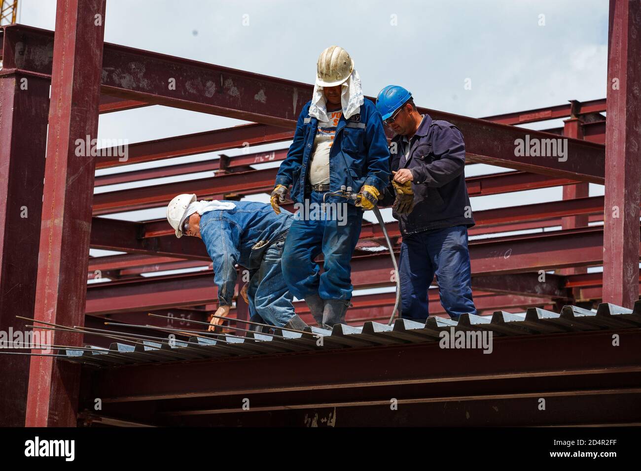 Shymkent, Kazakhstan. industrial building of chemical pharmaceutical plant Santo. Two workers and welder on roof makes reinforcement steel works. Stock Photo