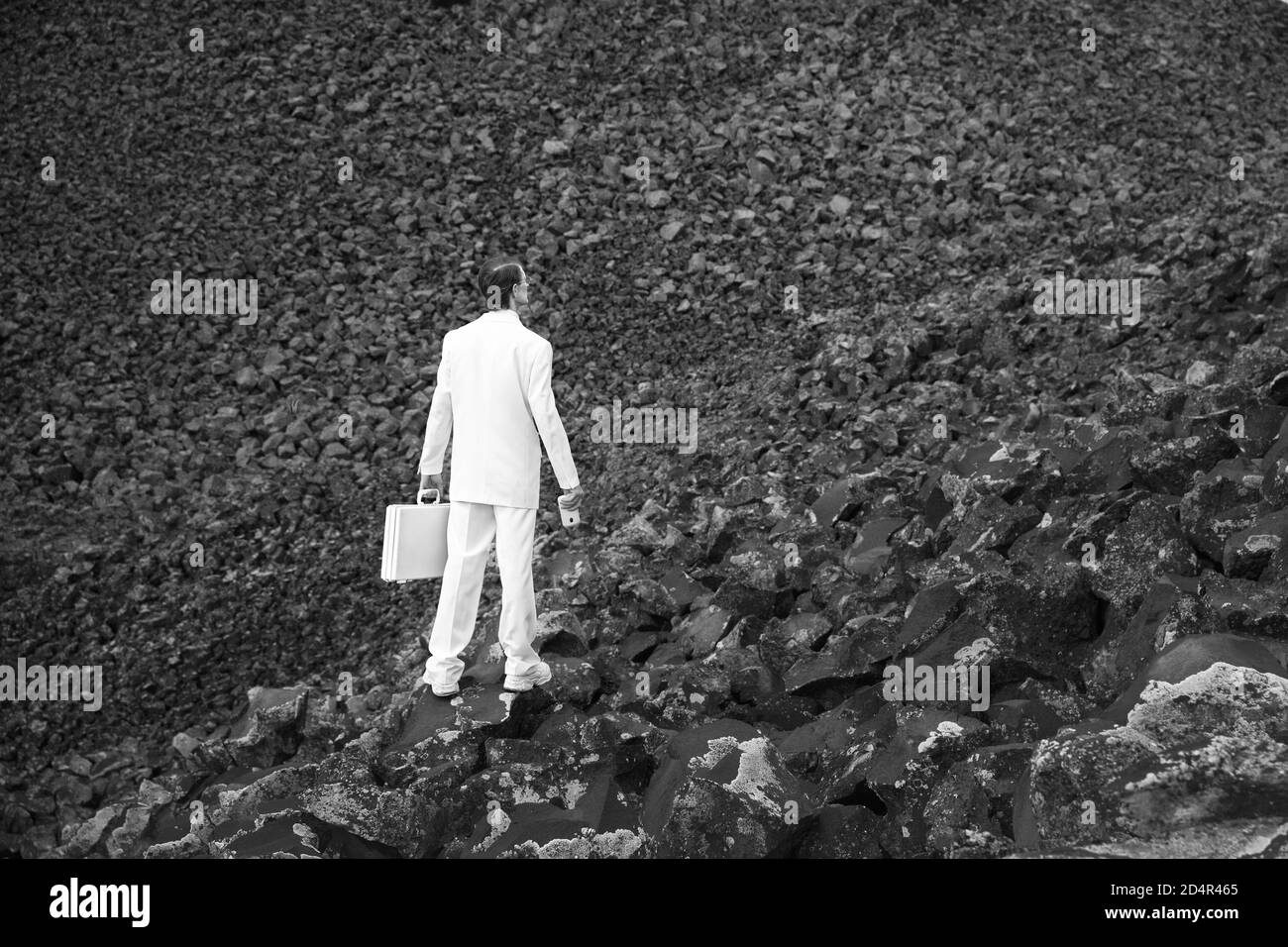 Businessman dressed in all white standing against an ominous, dark background of boulders. Stock Photo