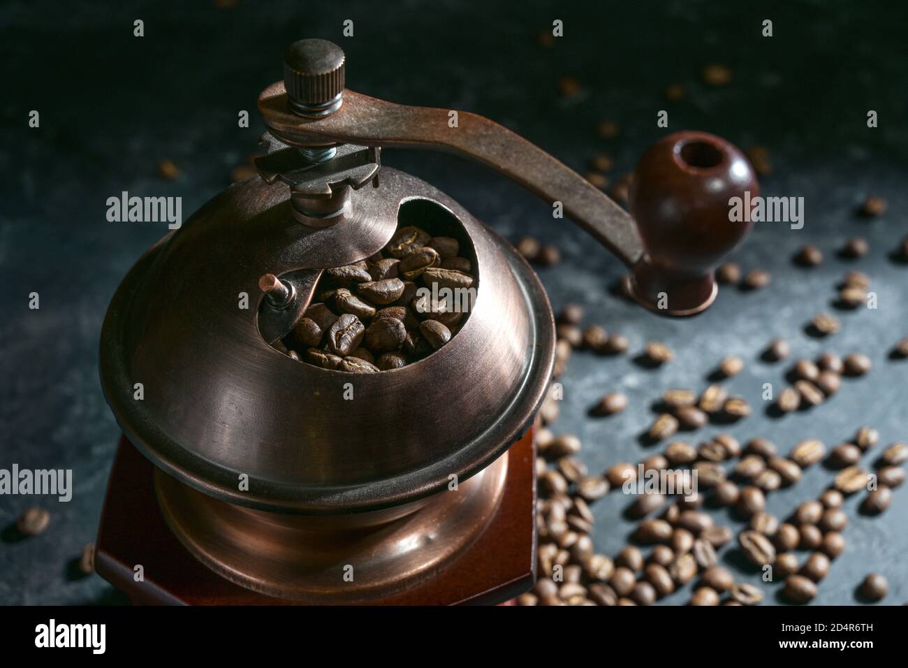 Part of a manual vintage coffee grinder and roasted beans on a dark ...