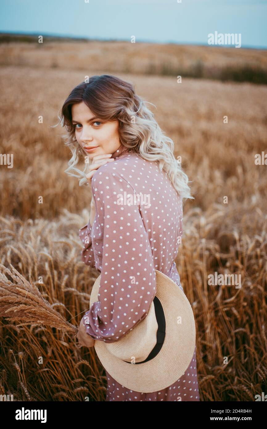 A young woman in a brown dress with white polka dots stands in a wheat ...