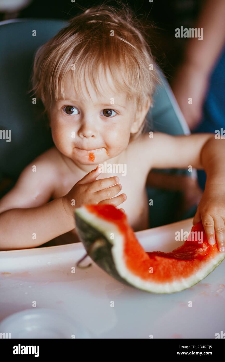 Happy toddler boy eating watermelon in his highchair Stock Photo