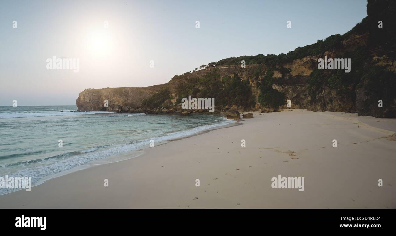 Sunlight sand beach at ocean bay waves aerial view. Amazing seascape with cliff coast and stones. Sumba island, Indonesia landscape at sunny summer day. Soft light sun shine over rock wall Stock Photo