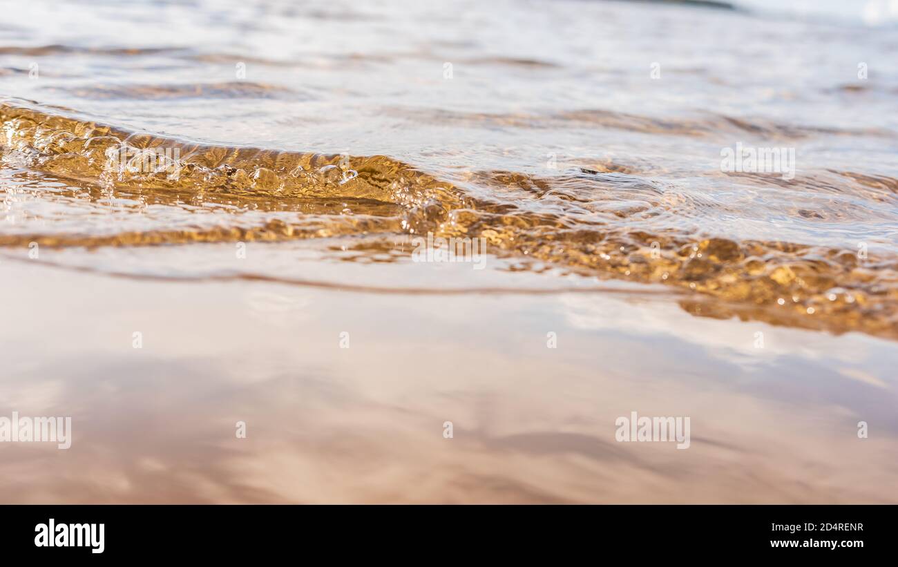 Small wave enters the beach during sunset which lights up the water with golden yellow color Stock Photo