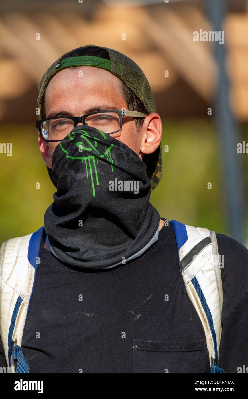Ellicott City, MD, USA 10/07/2020: A young caucasian male wearing a base ball hat backwards and a large cloth face mask is walking in the street. He h Stock Photo